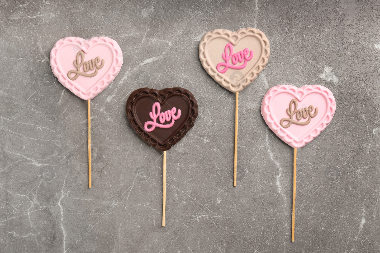 Photo of Different chocolate heart shaped lollipops with word Love on light grey marble table, flat lay