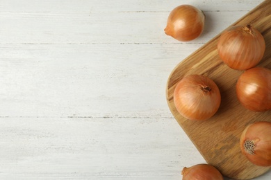 Photo of Ripe onions on white wooden table, flat lay with space for text