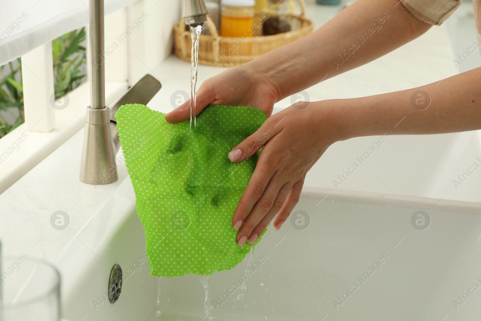 Photo of Woman washing beeswax food wrap under tap water in kitchen sink, closeup