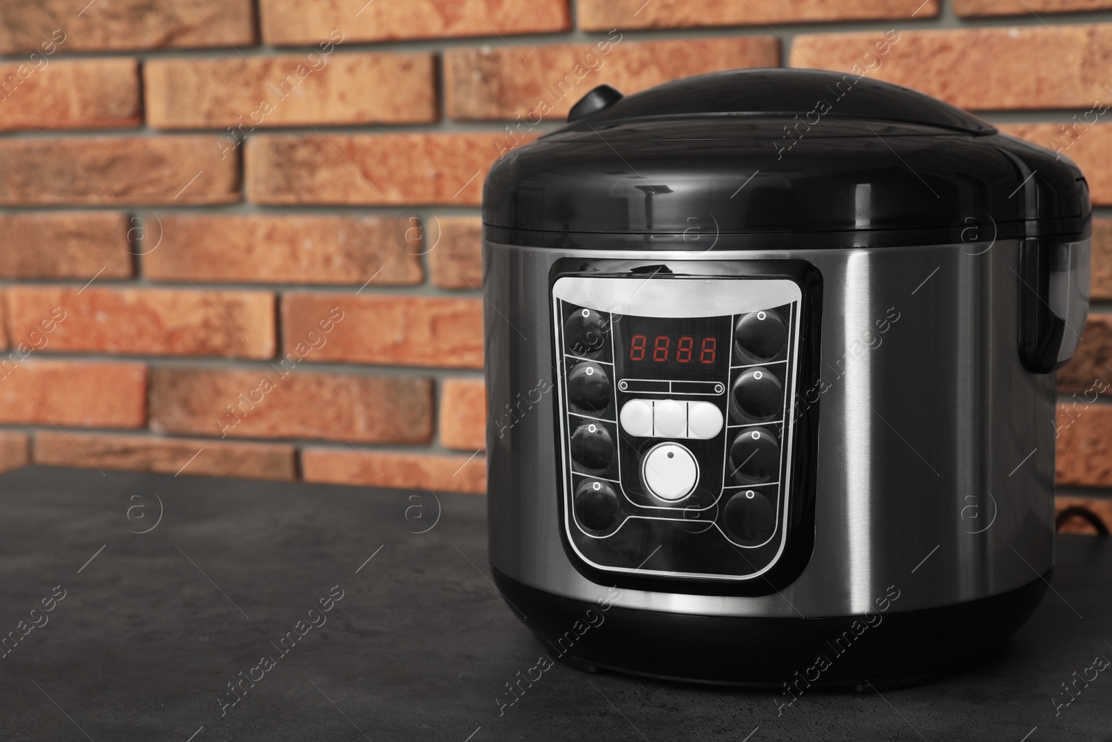 Photo of Modern electric multi cooker on table near brick wall. Space for text