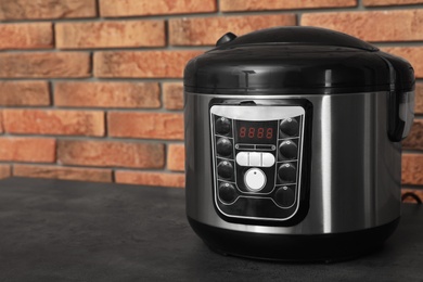 Photo of Modern electric multi cooker on table near brick wall. Space for text