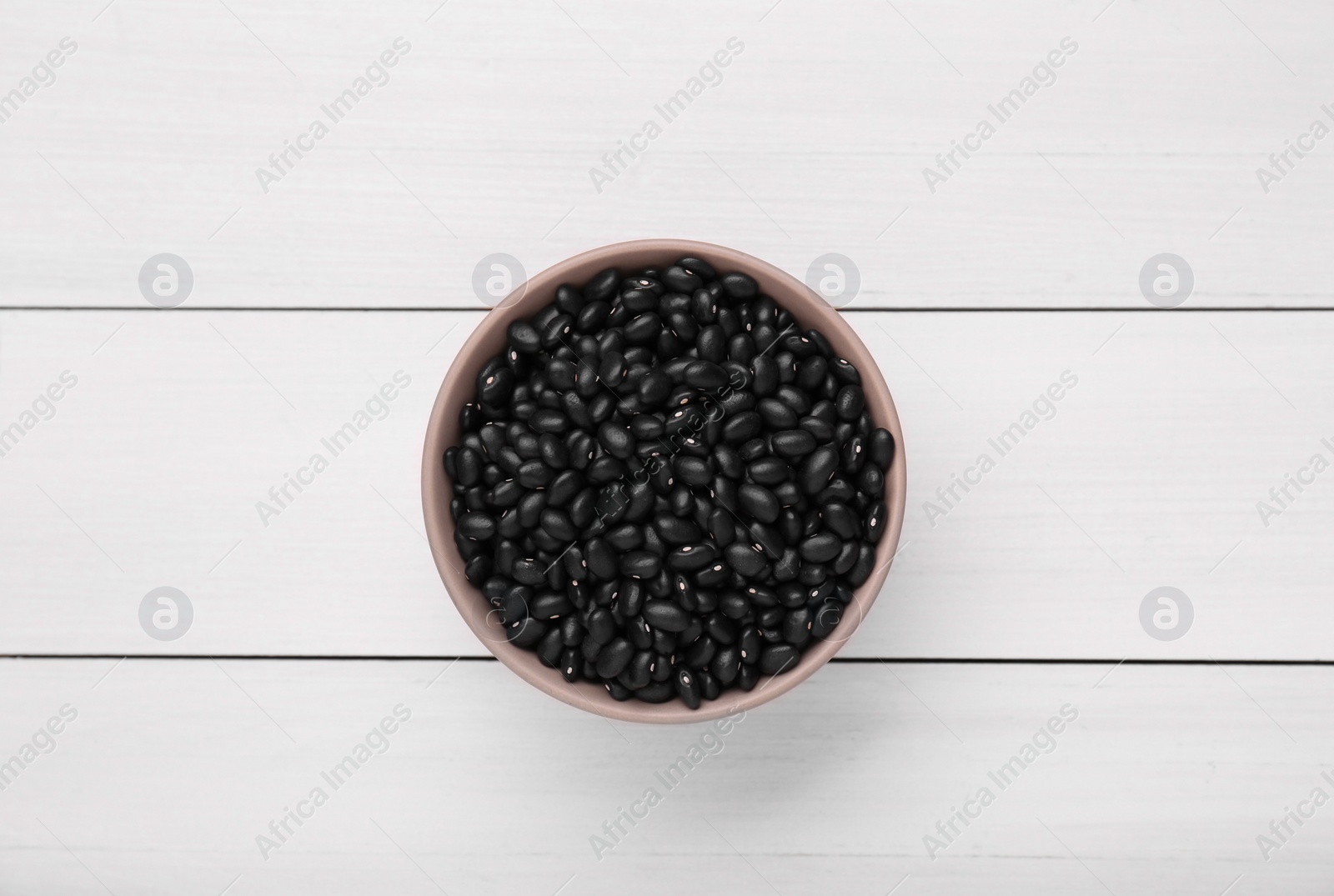 Photo of Bowl of raw black beans on white wooden table, top view