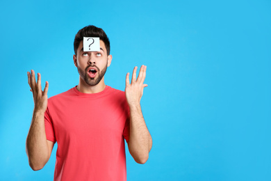 Emotional young man with question mark sticker on forehead against light blue background. Space for text
