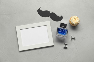 Photo of Empty photo frame, paper mustache, cupcake and men accessories on grey table, flat lay with space for text. Father's day celebration