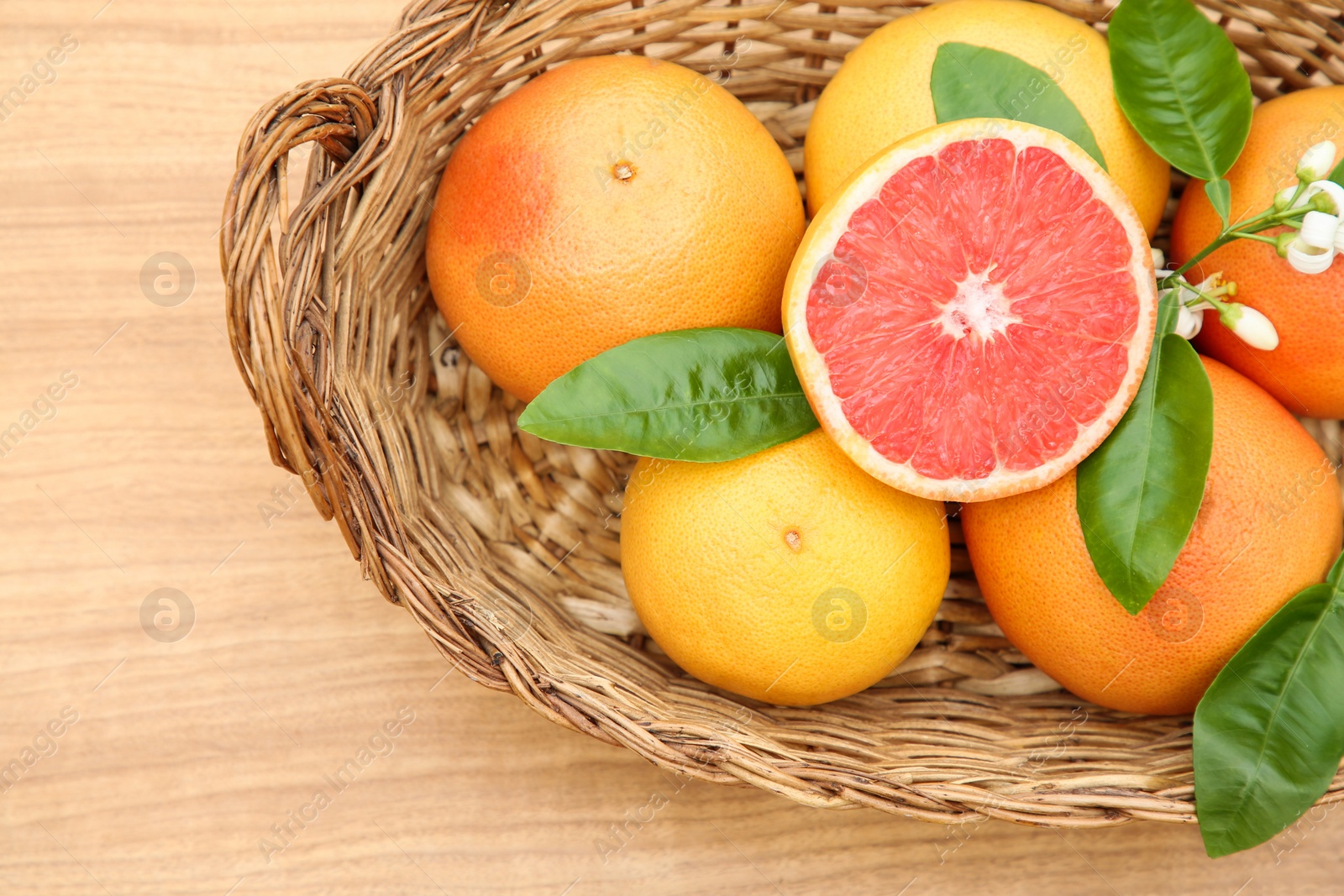 Photo of Wicker basket with fresh ripe grapefruits and green leaves on wooden table, top view