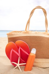 Straw bag, flip flops, starfish and sunscreen on beach
