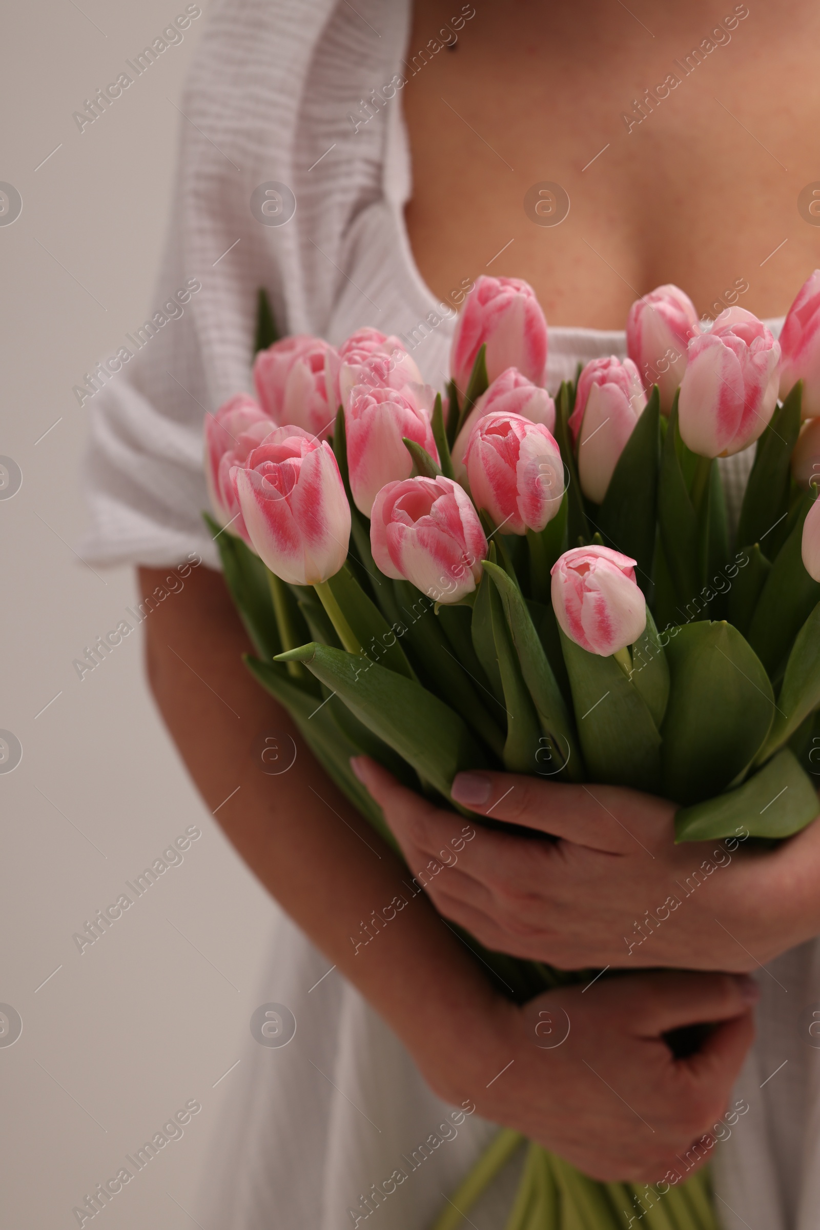 Photo of Woman with bouquet of beautiful fresh tulips on light grey background, closeup