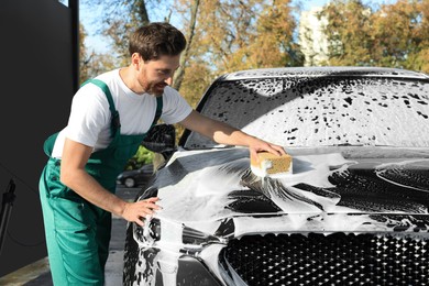 Worker washing auto with sponge at outdoor car wash