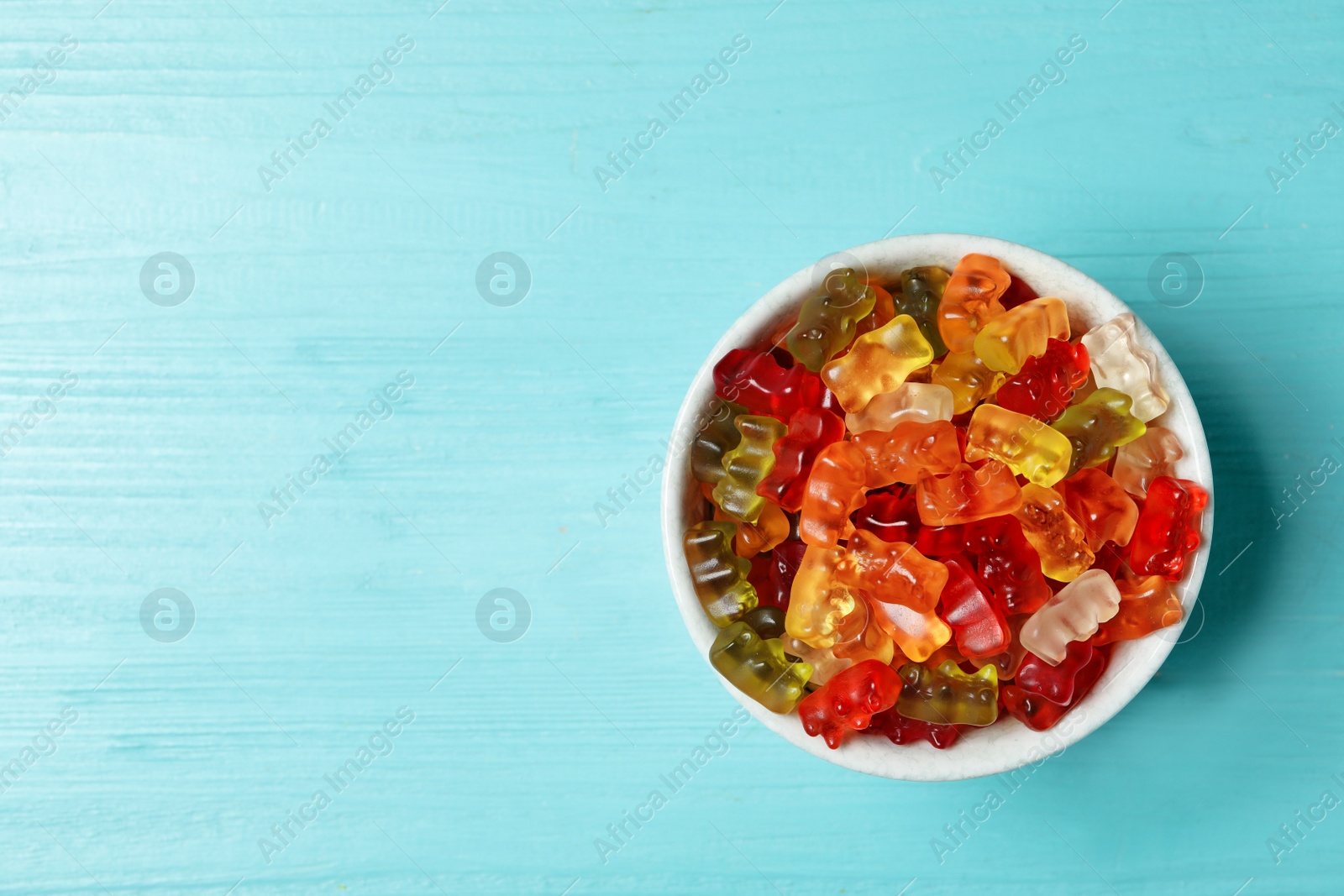 Photo of Bowl with delicious jelly bears on wooden table, top view. Space for text