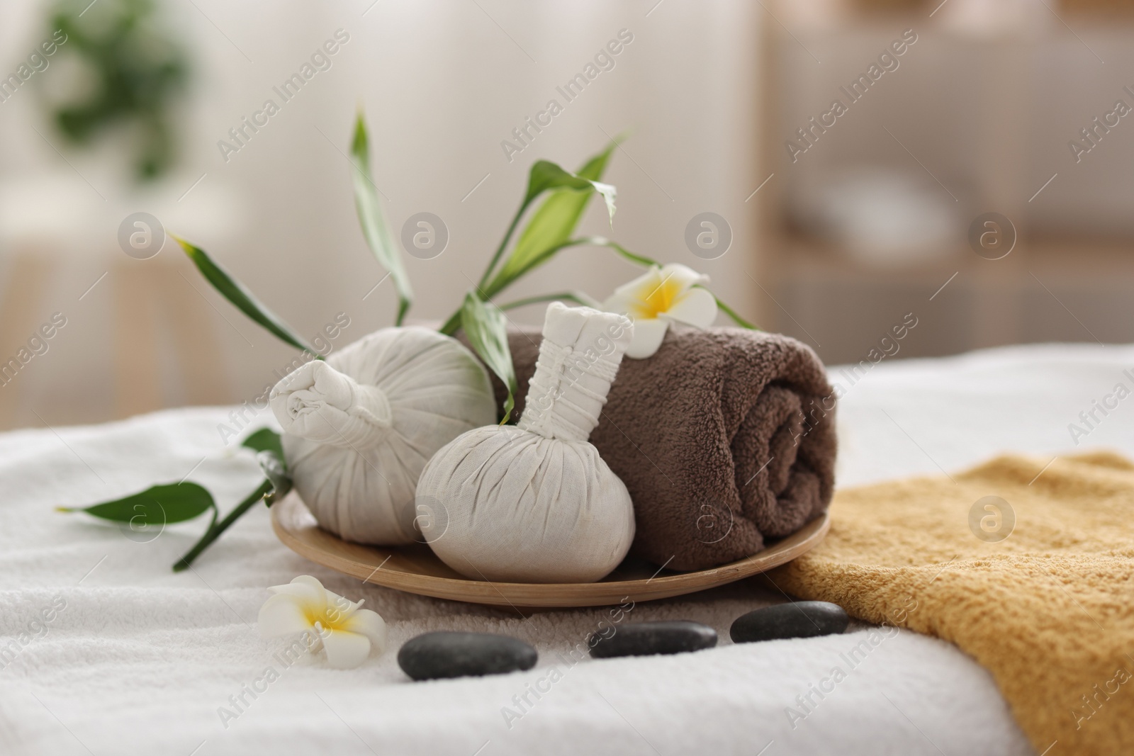 Photo of Spa stones, flowers and herbal bags on towel indoors