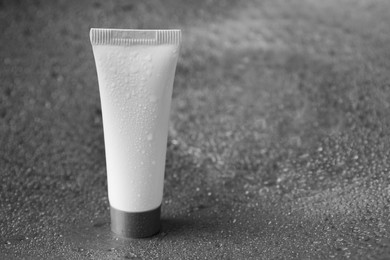 Photo of Moisturizing cream in tube on dark wet background, closeup. Space for text