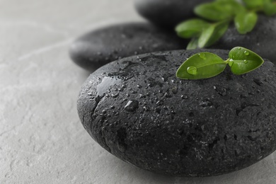 Spa stones and green leaves with water drops on grey table, space for text