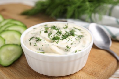 Photo of Tasty creamy dill sauce in bowl on wooden board, closeup