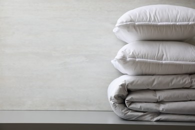 Photo of Soft folded blanket and pillows on light grey table, closeup. Space for text