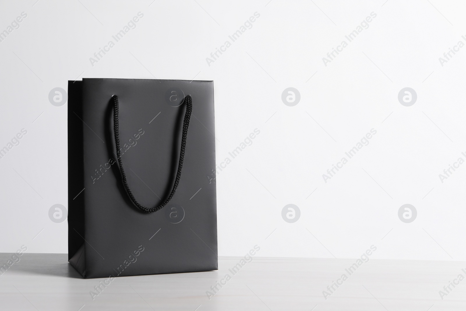 Photo of Black paper bag on white wooden table, space for text