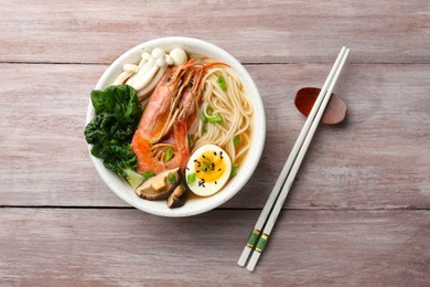 Photo of Delicious ramen with shrimps and egg in bowl and chopsticks on wooden table, top view. Noodle soup