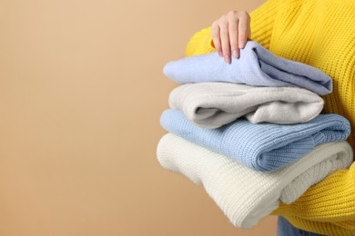 Photo of Woman with stack of casual sweaters on light brown background, closeup. Space for text