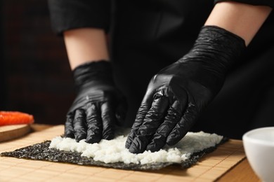 Photo of Chef in gloves making sushi roll at table, closeup