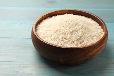 Photo of Raw basmati rice in bowl on light blue wooden table