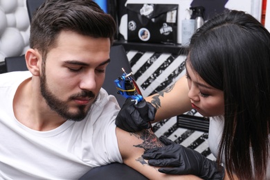 Photo of Professional artist making tattoo with machine in salon
