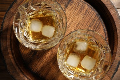 Glasses of whiskey with ice cubes on wooden barrel, top view