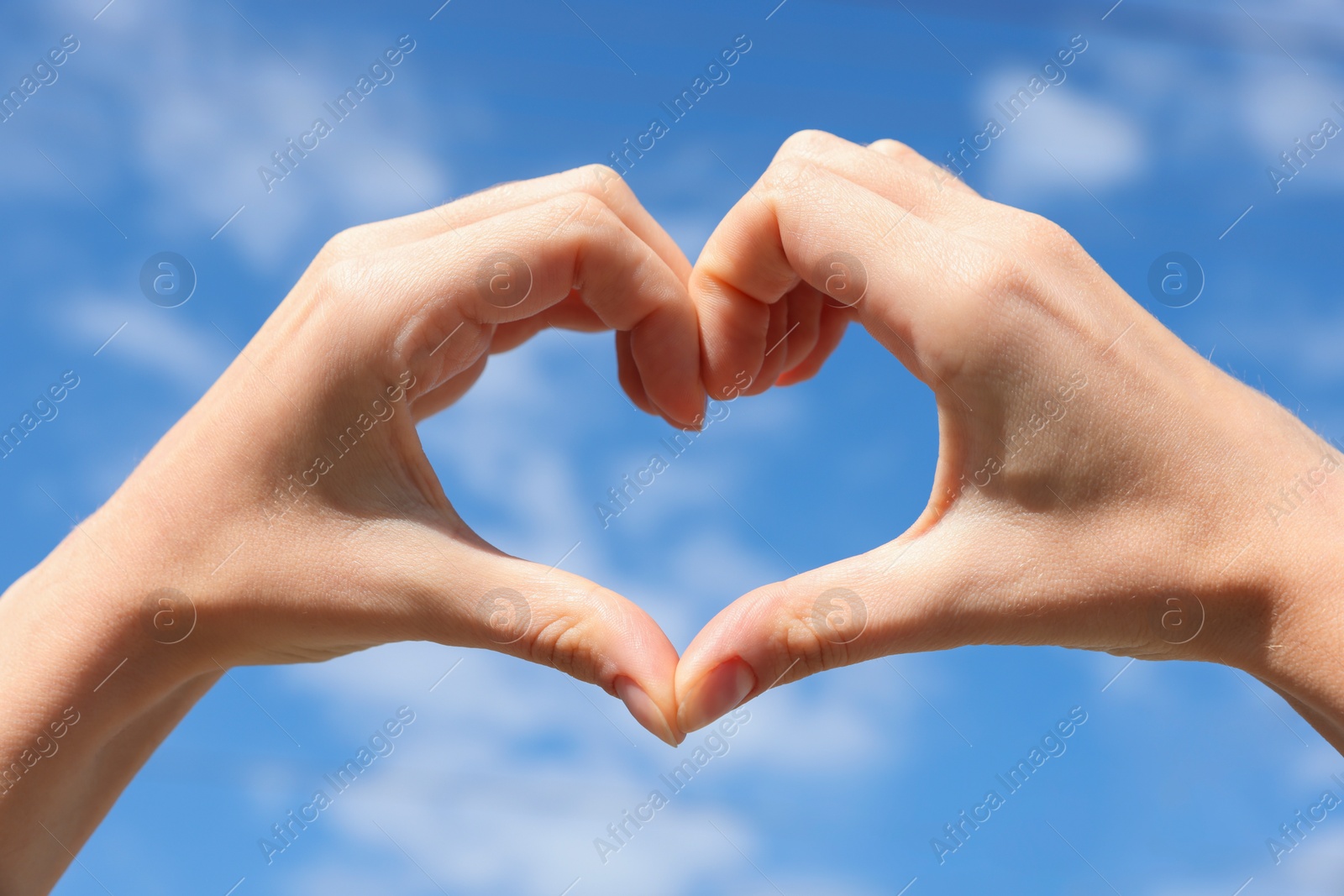 Photo of Woman making heart with hands against blue sky, closeup