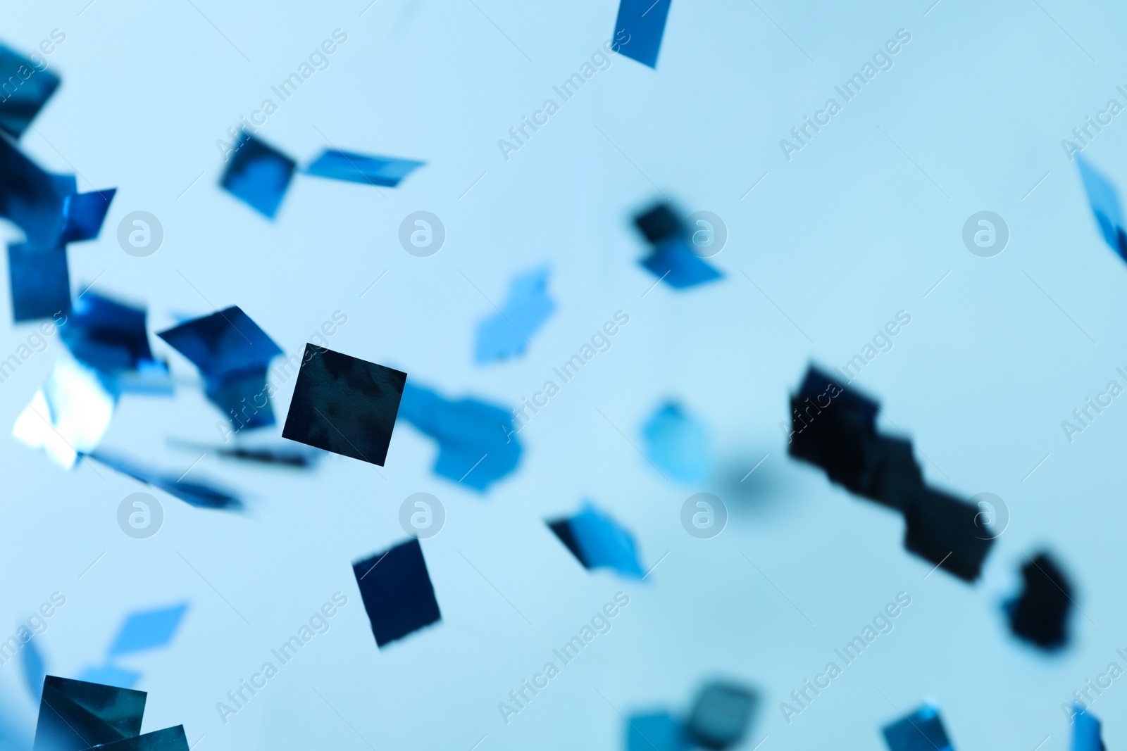 Photo of Shiny confetti falling down on light blue background