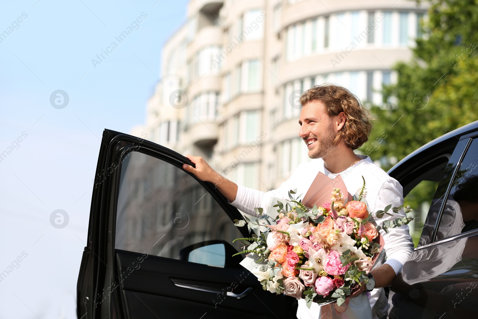 Photo of Young handsome man with beautiful flower bouquet near car on street