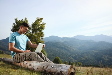 Photo of Man working with laptop in mountains on sunny day