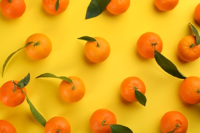 Photo of Fresh tangerines with green leaves on yellow background, flat lay