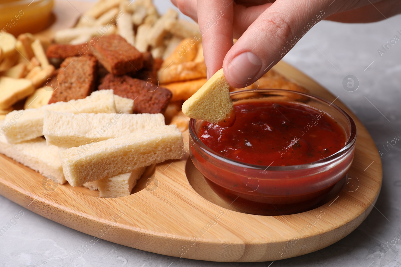 Photo of Woman dipping crispy rusk in sauce at light table, closeup