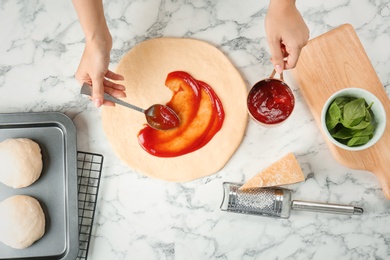 Photo of Woman spreading tomato sauce on pizza on table, top view