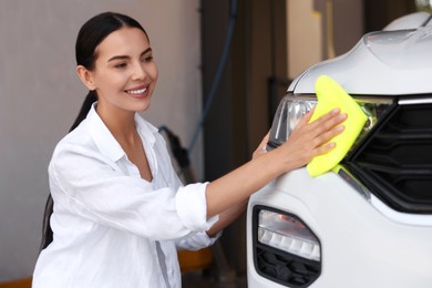 Photo of Happy woman cleaning headlight with rag at car wash