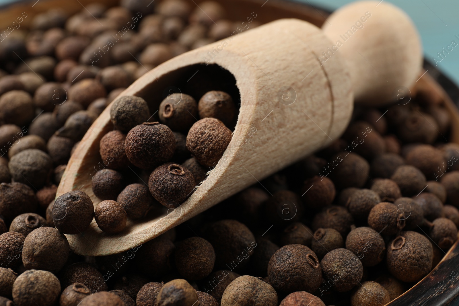 Photo of Aromatic allspice pepper grains in bowl and wooden scoop, closeup