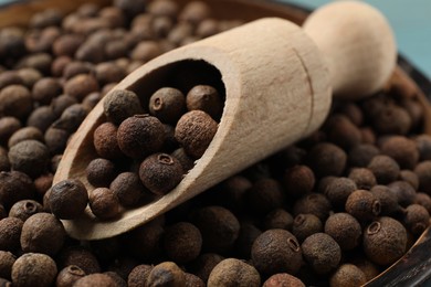 Aromatic allspice pepper grains in bowl and wooden scoop, closeup