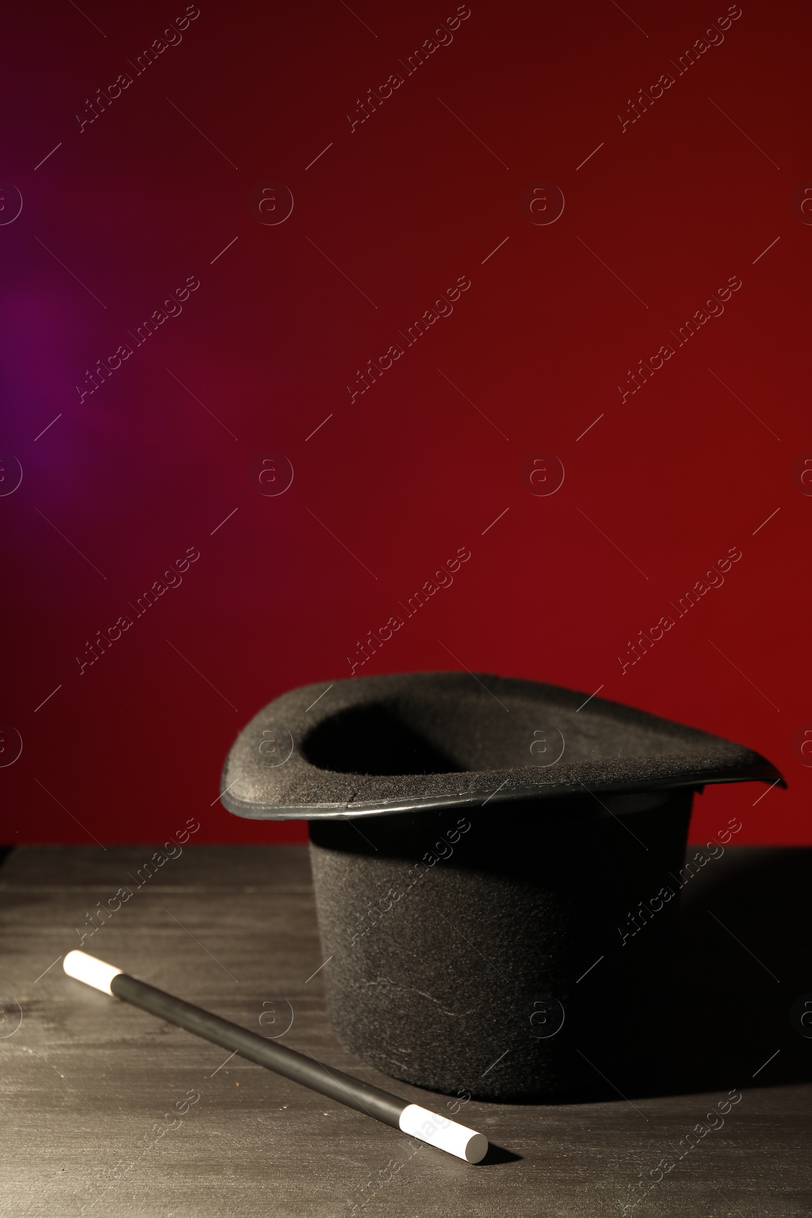 Photo of Magician's hat and wand on black wooden table against color background, space for text