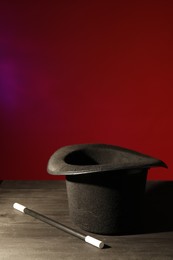 Photo of Magician's hat and wand on black wooden table against color background, space for text