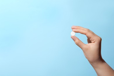 Woman holding pill on light blue background, closeup. Space for text