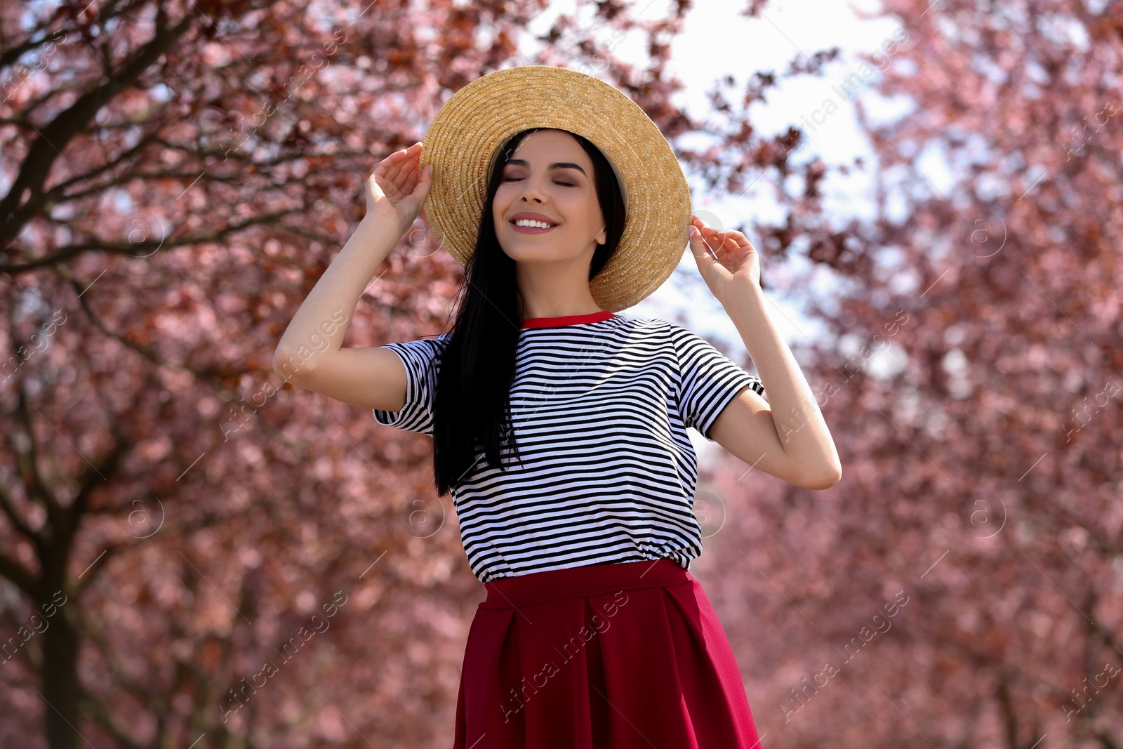 Photo of Pretty young woman with straw hat near beautiful blossoming trees outdoors. Stylish spring look