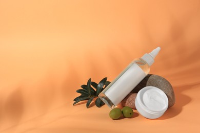 Cosmetic products and olives on orange background, space for text