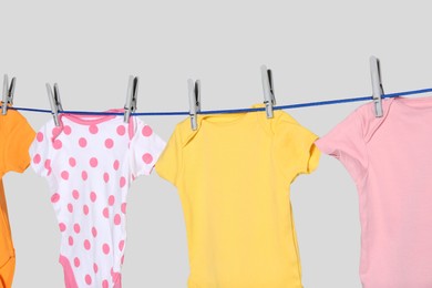 Photo of Colorful baby onesies drying on laundry line against light background, closeup