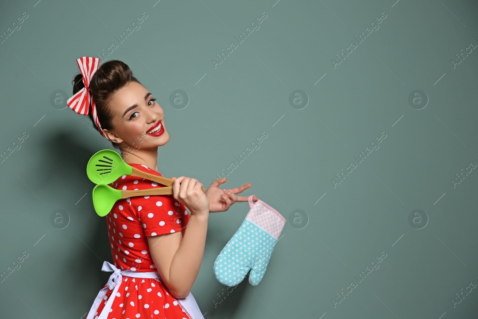 Photo of Funny young housewife with oven mitten and cooking utensils on color background