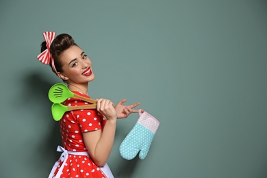 Funny young housewife with oven mitten and cooking utensils on color background