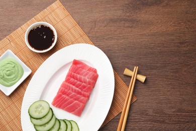 Photo of Tasty sashimi (pieces of fresh raw tuna), cucumber slices, soy sauce and wasabi on wooden table, flat lay