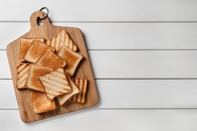 Board with slices of delicious toasted bread on white wooden table, top view. Space for text