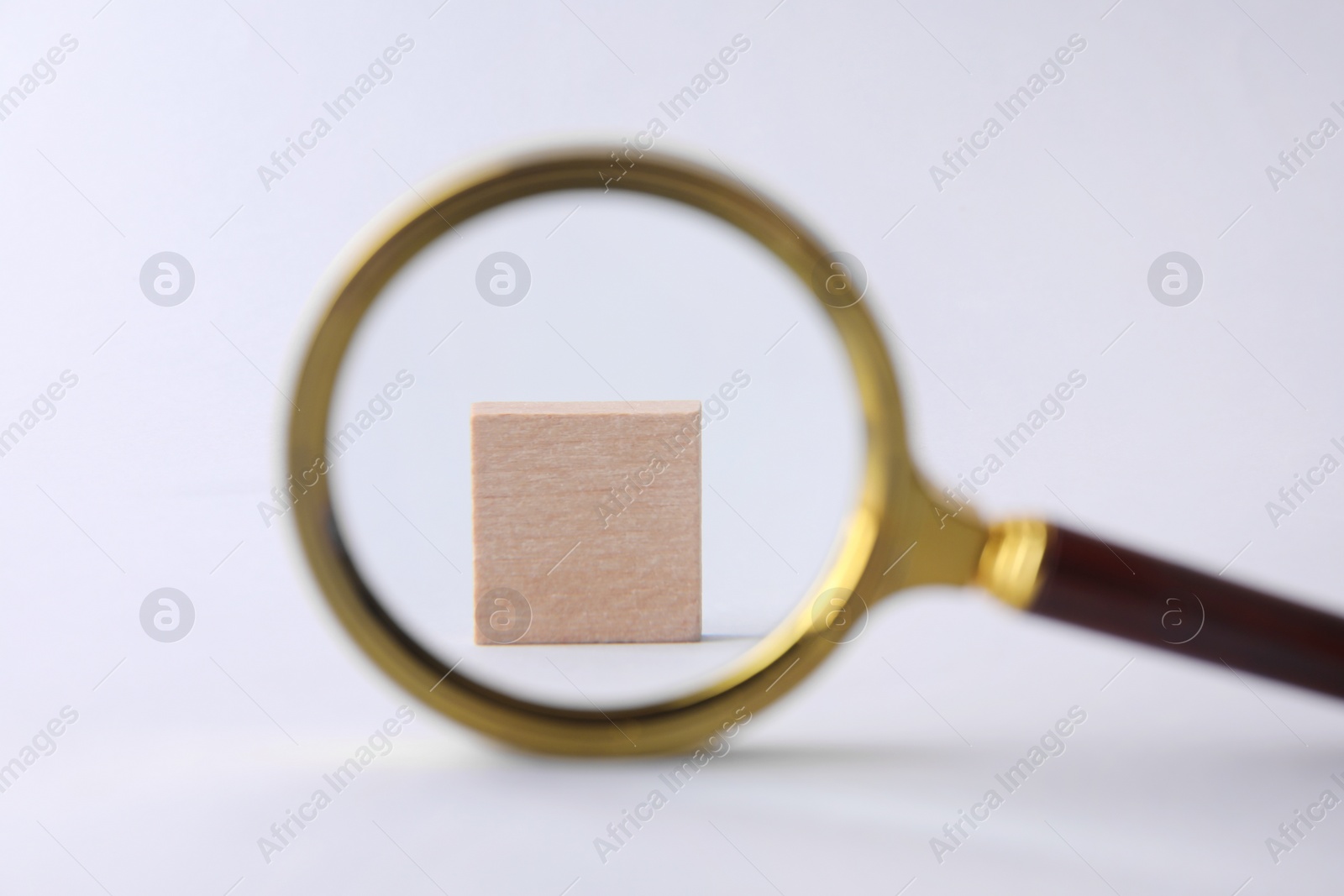 Photo of Wooden cube on white background, view through magnifying glass