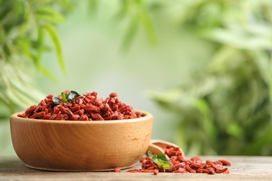 Photo of Bowl of dried goji berries on table against blurred background. Space for text