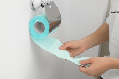 Photo of Woman taking toilet paper from roll holder in bathroom, closeup