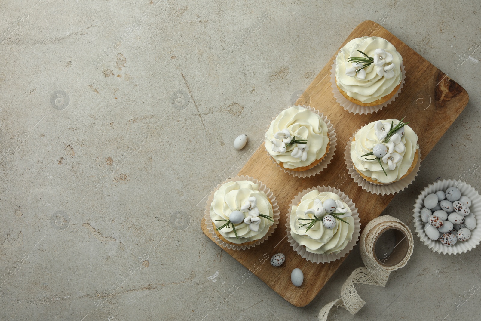 Photo of Tasty Easter cupcakes with vanilla cream, candies and ribbon on gray table, flat lay. Space for text