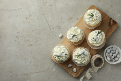 Photo of Tasty Easter cupcakes with vanilla cream, candies and ribbon on gray table, flat lay. Space for text